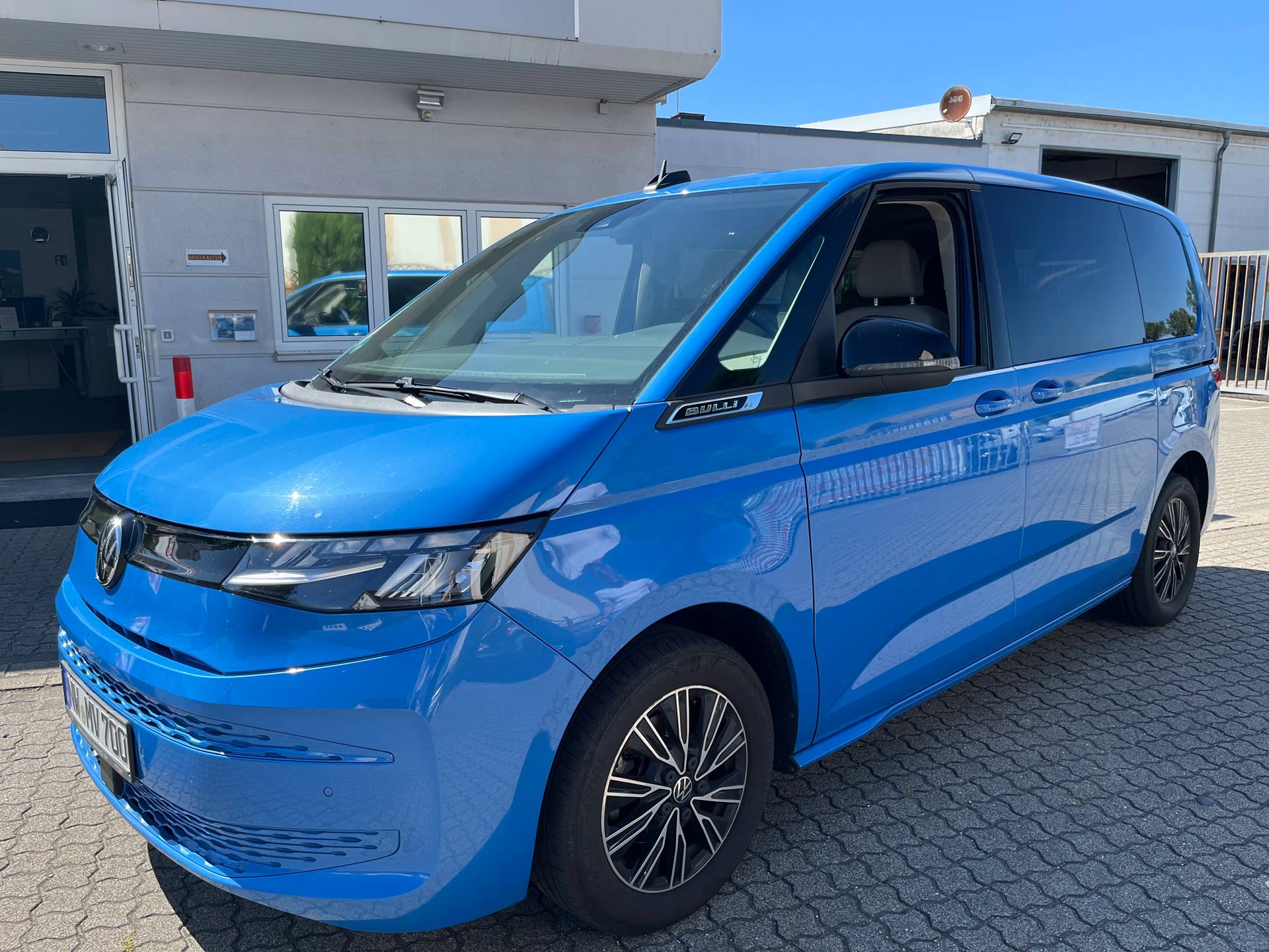 Blauer VW Bulli Transporter mit glaenzendem Lack vor einem Gebaeude geparkt