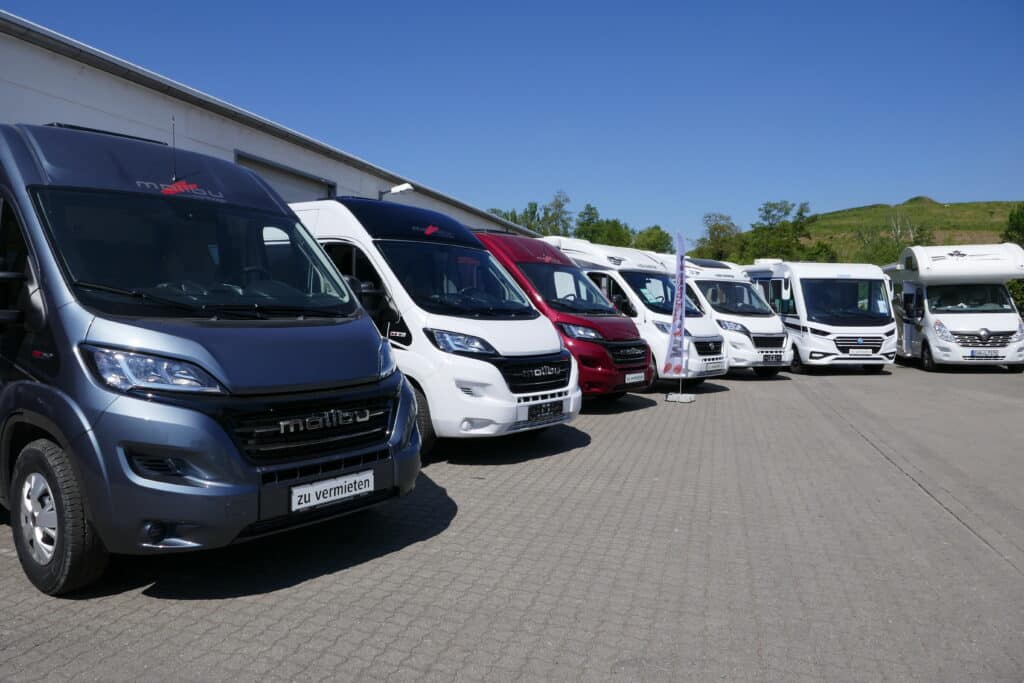 Mehrere Wohnmobile stehen in einer Reihe auf einem großen Parkplatz