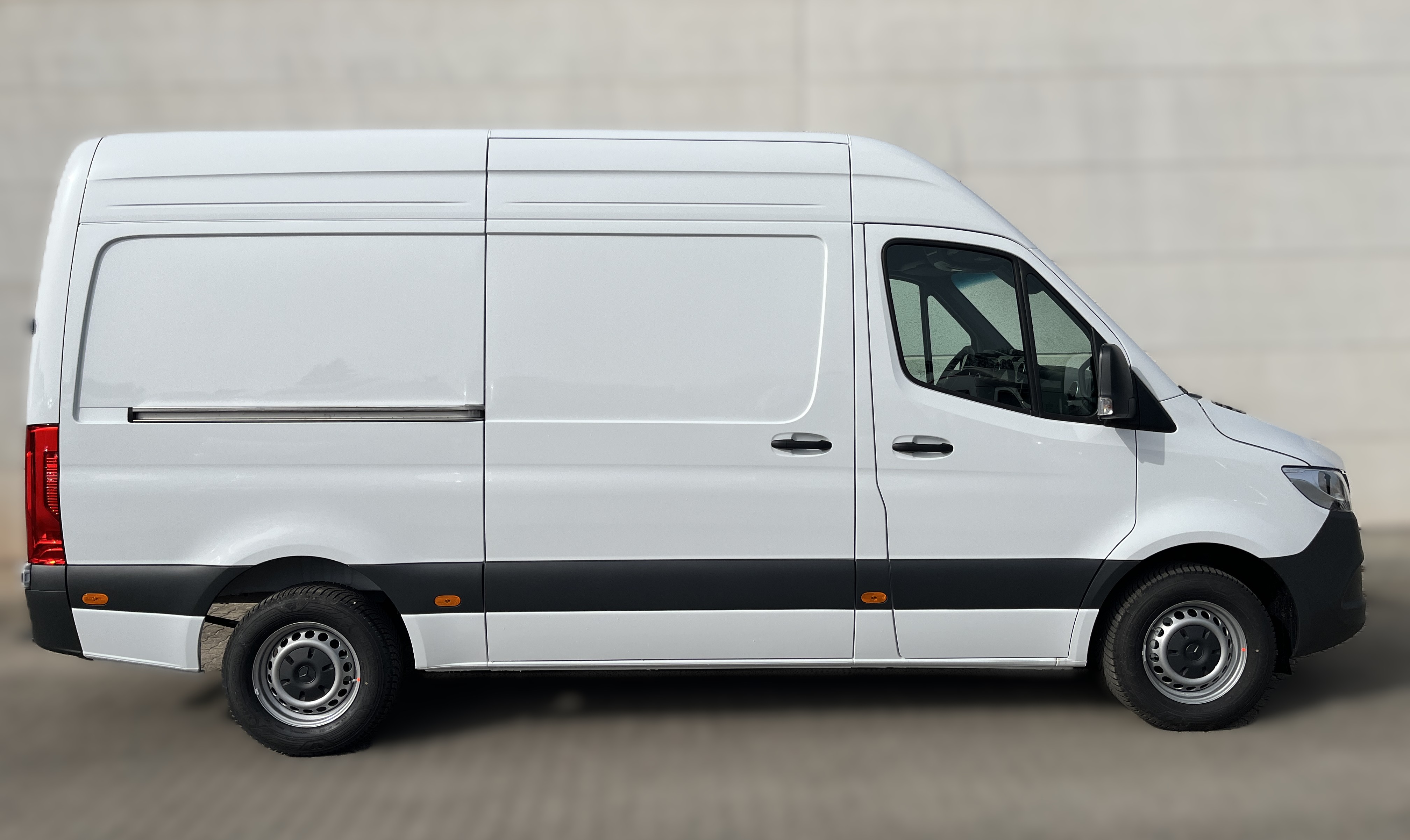 Ein weißer Lieferwagen steht seitlich vor einer grauen Wand auf gepflastertem Boden