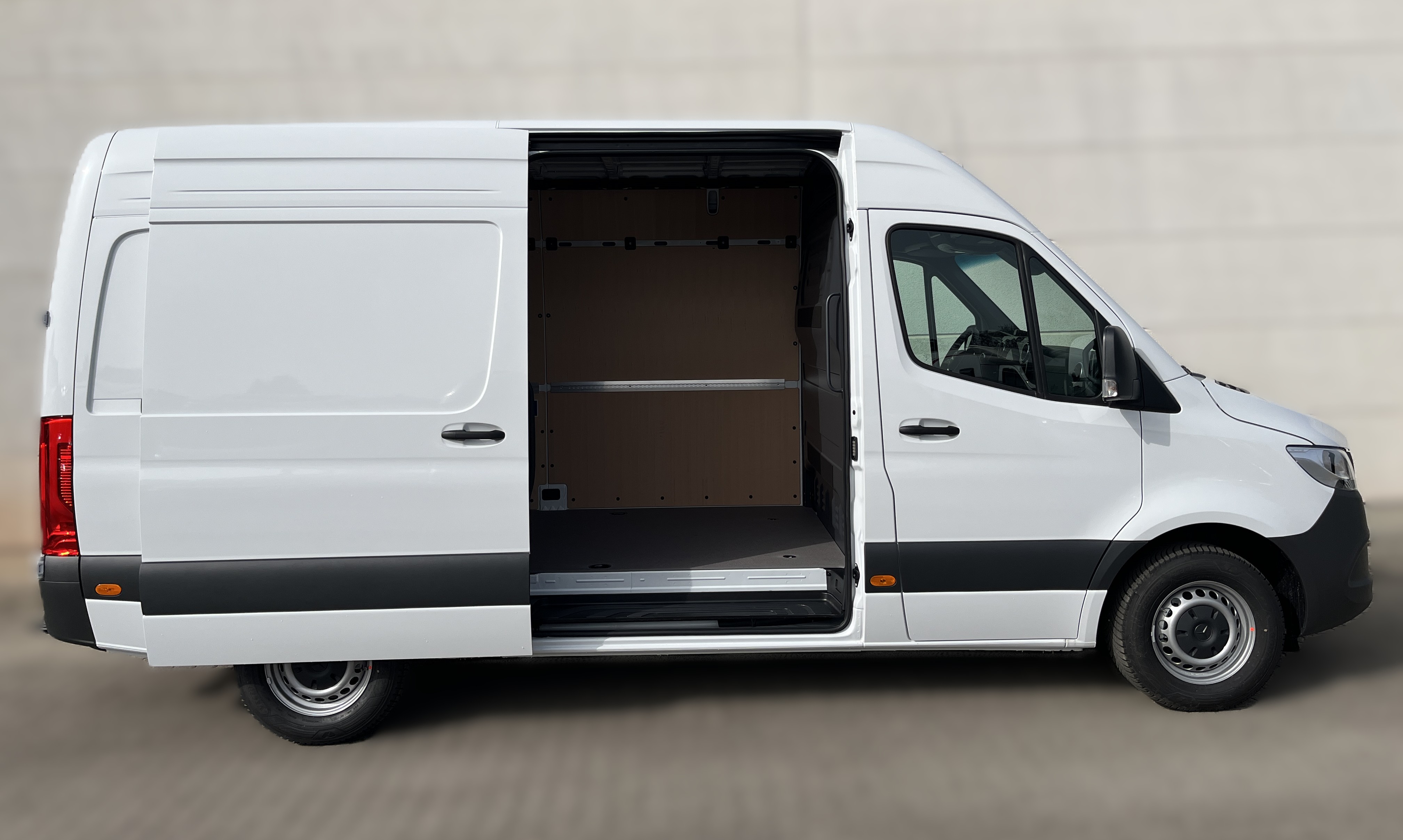 Ein weißer Lieferwagen mit seitlich geöffneter Tür und leerem Laderaum vor Betonwand