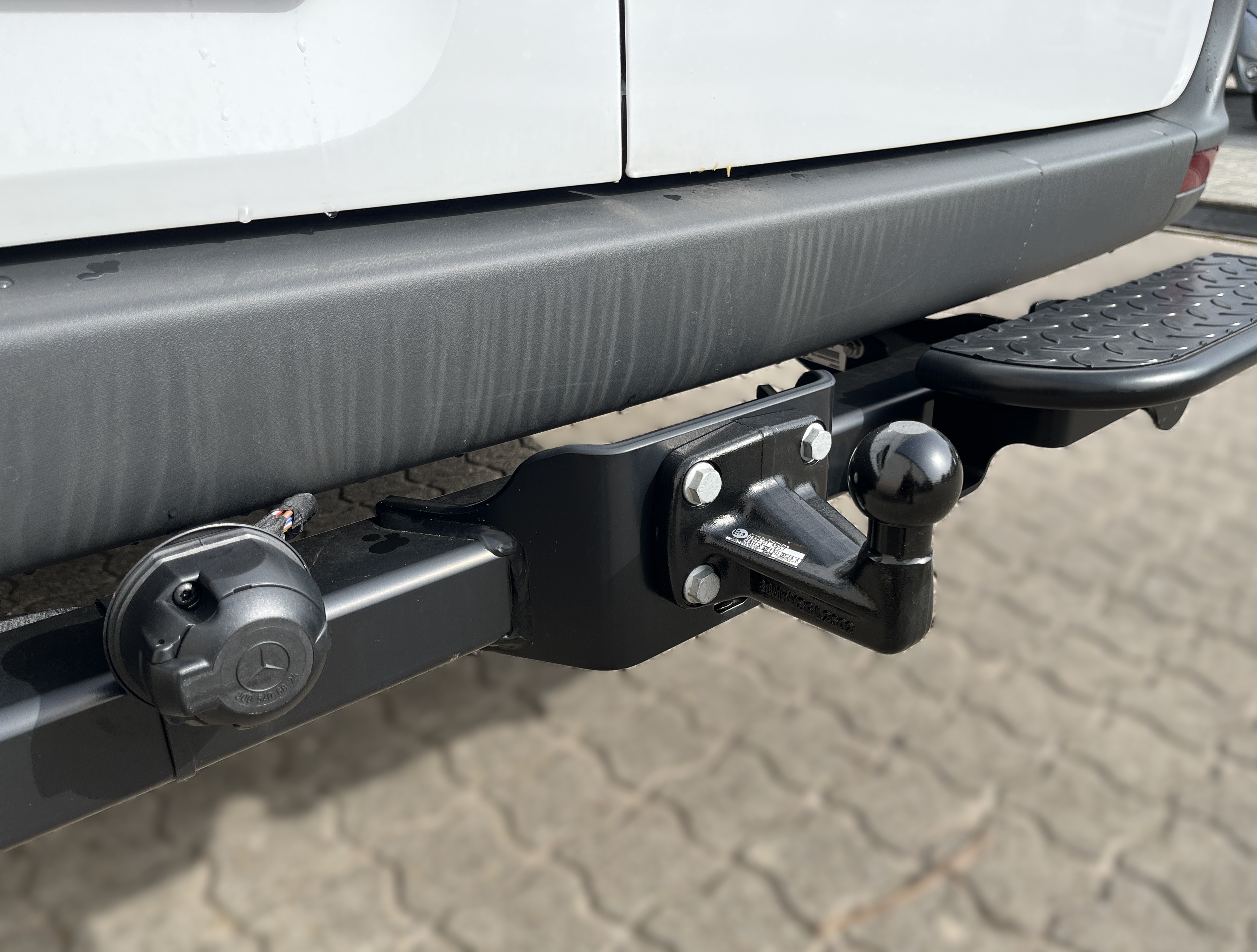 Anhängerkupplung an einem weißen Fahrzeug mit mattem Stoßfänger und Steckdose