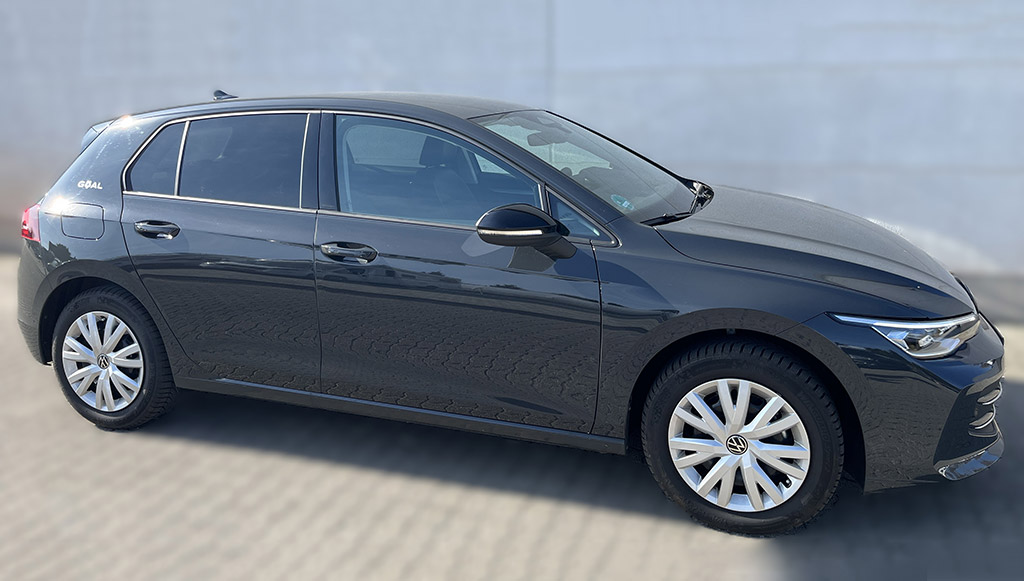 Ein schwarzer Volkswagen Golf steht seitlich auf gepflastertem Boden vor grauer Wand