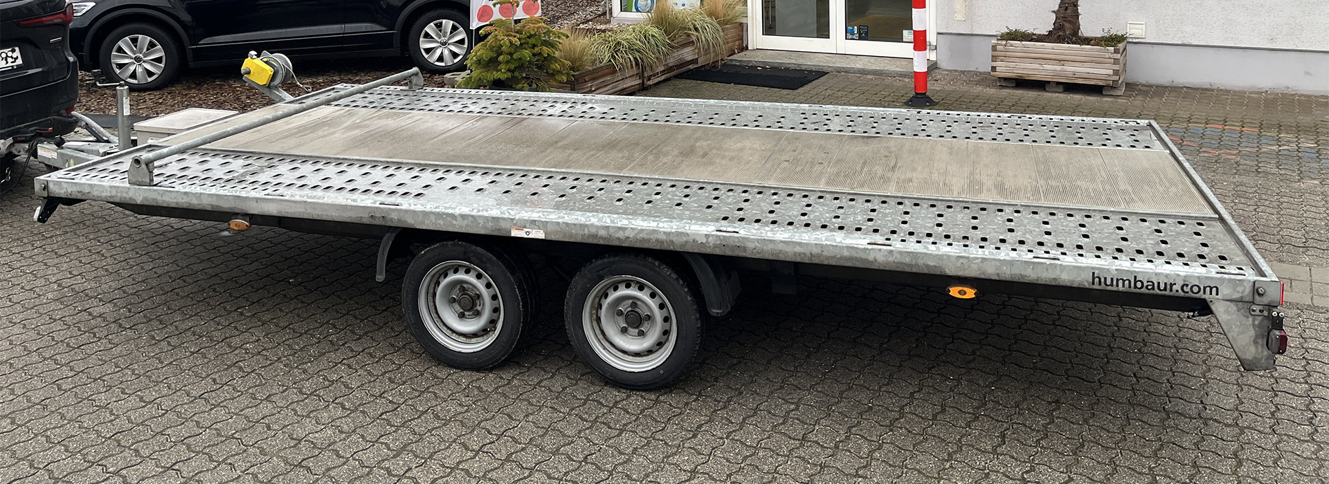 Ein leerer silberner Anhänger mit zwei Achsen steht auf einem gepflasterten Parkplatz