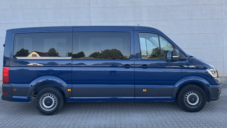 Ein blauer Transporter mit getönten Fenstern steht vor einer grauen Wand im Freien